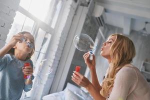 Family bonding. Mother and daughter blowing soap bubbles while spending time at home photo