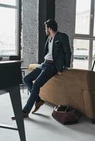 Thinking about... Full length of thoughtful young man in full suit looking away while leaning on the sofa photo