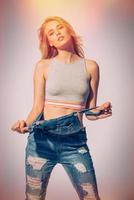 Casually beautiful. Studio shot of beautiful young woman taking off her jeans overall and looking at camera photo