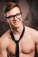 Shirtless business. Handsome young man in eyewear and necktie looking at camera and smiling while standing against metal background photo