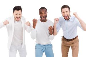 Men cheering. Three happy young men in smart casual wear expressing positivity and gesturing while standing against white background photo