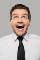 Wonderful news. Happy young man in shirt and tie smiling and looking up while standing against grey background photo