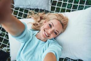 Top view of beautiful young smiling woman making selfie while relaxing in big hammock photo