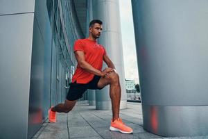 Charming young man in sports clothing making a lunge during his sport training while exercising outdoors photo