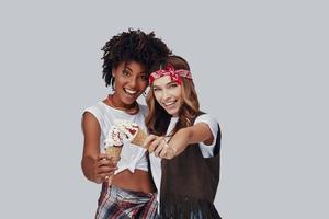 Two attractive young women looking at camera and smiling while standing against grey background photo