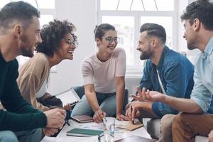 Group of modern young people discussing business and smiling while sitting in the office together photo