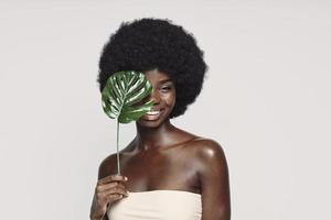 Portrait of beautiful young African woman holding plant near face and smiling photo