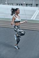 Best cardio ever. Beautiful young woman in sports clothing skipping rope while exercising outdoors photo