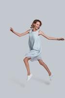 Beauty in the mid-air. Full length of playful young woman gesturing and keeping mouth open while jumping against grey background photo