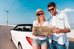 Free to choose our destinations. Joyful young couple examining map while standing against their white convertible photo