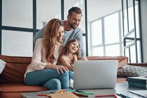 joven y hermosa familia con una niñita que se une y sonríe mientras usa una laptop en casa foto