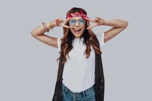 Attractive stylish young woman looking at camera and sticking out tongue while standing against grey background photo