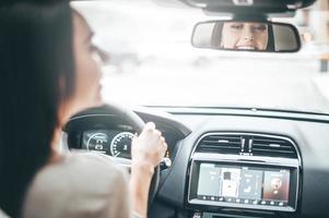 conductor en el espejo retrovisor. vista trasera de una joven atractiva con ropa informal mirando en el espejo retrovisor y sonriendo mientras conduce un camión foto