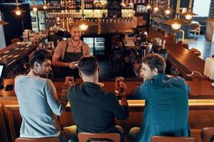 vista superior de jóvenes relajados con ropa informal bebiendo cerveza mientras se sientan en el pub foto