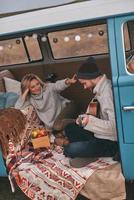 admirado por él. vista superior de un apuesto joven tocando la guitarra para su bella novia mientras se sienta en una mini furgoneta azul de estilo retro foto