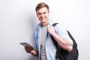 Modern student. Handsome young student holding digital tablet and smiling while standing against grey background photo