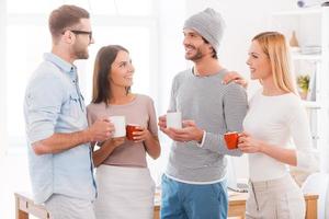 charla de pausa para el café. grupo de empresarios con ropa informal inteligente sosteniendo tazas de café y sonriendo mientras están cerca unos de otros en la oficina foto