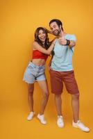 Full length of beautiful young couple smiling while standing against yellow background photo