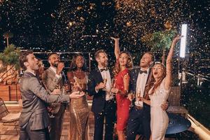 Group of happy people in formalwear having fun together with confetti flying all around photo
