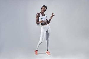 Happy young African woman in sports clothing holding bottle with water and gesturing photo