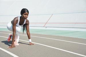hermosa joven africana parada en la posición inicial en la pista de atletismo al aire libre foto