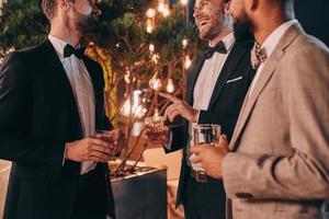 primer plano de tres hombres bien vestidos bebiendo whisky y comunicándose mientras pasan tiempo en la fiesta