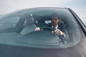 Busy day. Handsome young man in full suit looking straight while driving a car photo