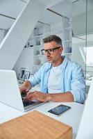 Confident mature man working on laptop while sitting at the office desk photo