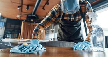 Busy man in protective face shield cleaning table in restaurant photo