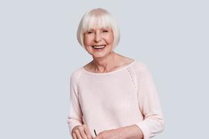 In her own style. Beautiful senior woman looking at camera and smiling while standing against grey background photo