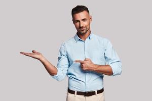 Solution is here. Handsome young man pointing copy space and looking at camera while standing against grey background photo