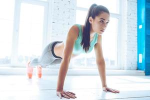 How long can you hold a plank Full length of young beautiful woman in sportswear doing plank while standing in front of window at gym photo