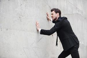 Trying to come out of stress. Frustrated young man in formalwear pushing the wall while standing outdoors photo