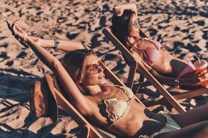 gran bronceado vista superior de atractivas mujeres jóvenes sonriendo y tomando el sol mientras descansan en sillas al aire libre en la playa foto