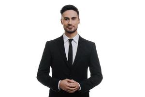 Confidence and charisma.  Handsome young man in full suit holding hands clasped and looking at camera while standing against white background photo