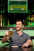 Man in beer pub. Cheerful young man holding a mug with beer and smiling while sitting in bar photo