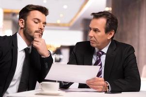 discutiendo contrato. dos hombres de negocios en ropa formal discutiendo algo mientras uno de ellos le muestra un papel a otro foto