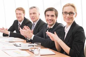 Applauding to you. Four people in formalwear sitting together at the table and applauding you photo