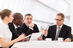 reunión de negocios. gente de negocios en ropa formal discutiendo algo mientras se sientan juntos en la mesa foto