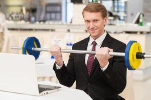 I choose healthy lifestyle. Smiling young red hair man in formalwear sitting at the restaurant and holding a dumbbell photo