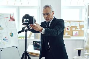 Senior man in elegant business suit adjusting video camera while making social media video photo