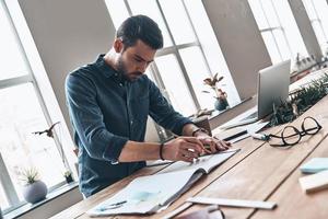 Putting ideas into something real. Concentrated young man drawing with ruler and pencil while working in the creative working space photo