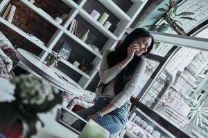 Talking about business. Attractive young smiling woman talking on smart phone and looking over her shoulder while standing in restaurant photo
