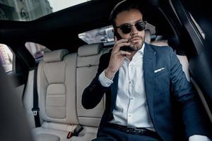 Discussing business details. Handsome young man in full suit talking on his smart phone while sitting in the car photo