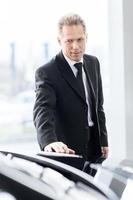 Making a right choice. Confident grey hair man in formalwear examining car at the dealership photo