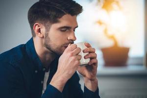 Enjoying his fresh coffee. Close-up part of handsome young man drinking coffee while sitting on the couch at home photo