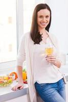 Taking a break while cooking. Attractive young woman holding glass with white wine and smiling while standing in the kitchen photo