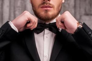 Tying a bow tie. Cropped image of handsome young beard man in formalwear adjusting his bow tie photo
