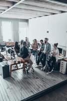 Group of young professionals.  Full length top view of young modern people in smart casual wear discussing something while standing behind the glass wall in the creative office photo