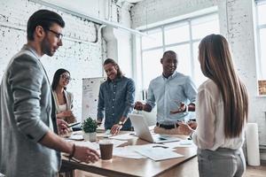 Discussing risky ideas. Group of young modern people in smart casual wear discussing business while standing in the board room photo